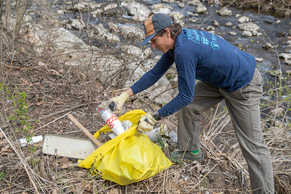 man cleaning up trash from stream bank