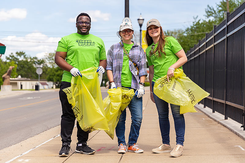 three young adults with yellow trash bags posing on roadway bridge