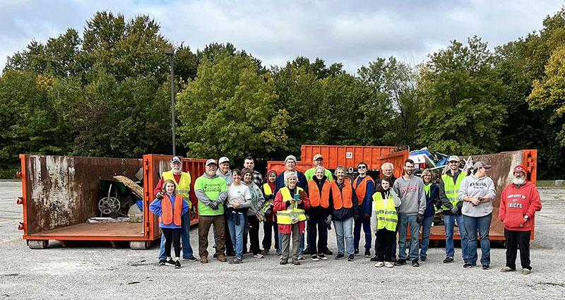 group of twenty plus volunteers stands in front of several orange trash dumpsters