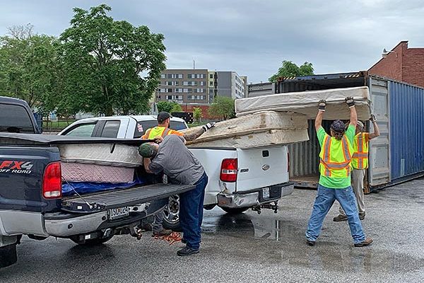 four men unloading old mattresses from two pickup trucks