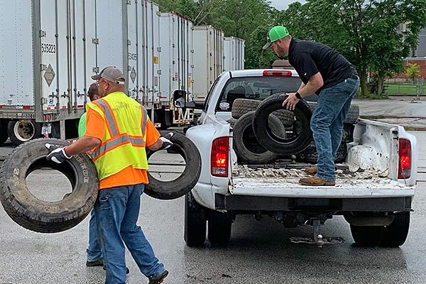 two men unloading old tires from a white pickup