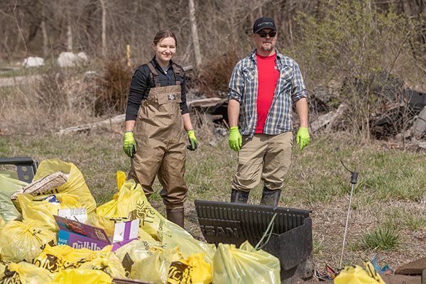 woman and man pose behind pile of trash gathered from stream and trail