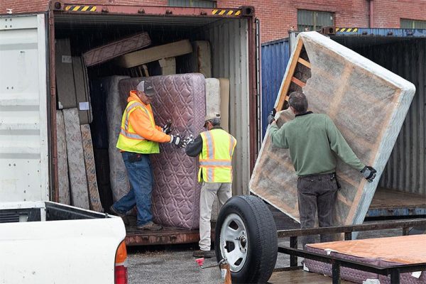 three men putting old mattresses into a storage trailer